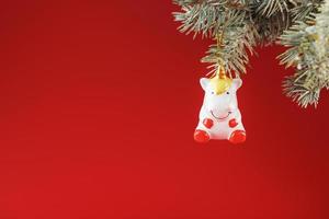 figura de cerámica de un unicornio sobre una rama de abeto, sobre un fondo rojo. espacio libre para texto. foto