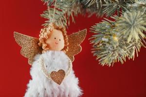 juguete de ángel de navidad hecho a mano en un árbol de navidad sobre un fondo rojo. foto