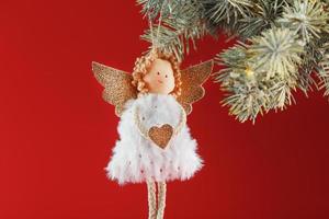 juguete de ángel de navidad hecho a mano en un árbol de navidad sobre un fondo rojo. foto