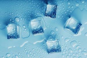 Ice cubes with drops of melt water water on a blue background, top view. photo