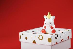 A little figure of a unicorn on the box with a gift on a red background. photo