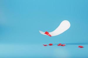 Sanitary pad in flight on a blue background with fallen petals of red flowers. Concept of the beginning of menopause. photo