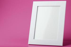marco de fotos blanco con un espacio vacío sobre un fondo rosa.