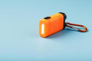 An orange led flashlight with a carabiner glows on a blue background. photo