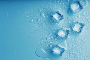 cubos de hielo con gotas de agua esparcidas sobre un fondo azul, vista superior. foto