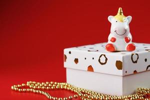 Unicorn figurine on a gift box with gold beads on a red background with free space. photo