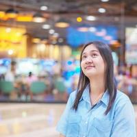 tome una foto de una mujer medio asiática con una camisa de mezclilla en una tienda por departamentos. fingiendo estar pensando en lo que quieres comprar.