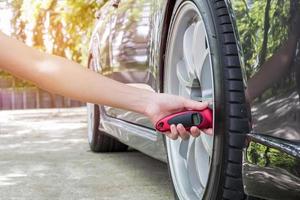 las mujeres usan el indicador de neumáticos para comprobar la presión de aire de los neumáticos en la carretera, el servicio básico comprueba la seguridad en la carretera con el jardín foto