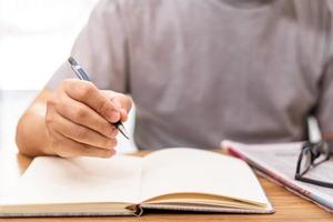 Close up hand a man hold pencil for write on the note book and newspaper glasses on wood table photo