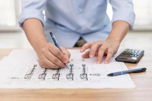 Engineering work concept  Close up hand a use pencil mark CAD drawing and calculator in Calculating document on the wood table photo