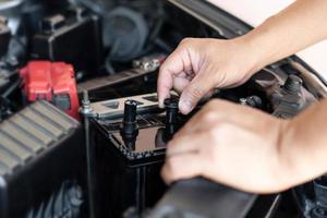 un hombre abre la tapa de la batería adicional para agregar destilado, mantenimiento e inspecciones para prolongar la vida útil de la batería del automóvil foto