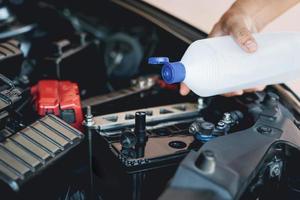 un hombre sostiene y agrega agua para destilar el mantenimiento de la batería del automóvil y las inspecciones para prolongar la vida útil del automóvil foto