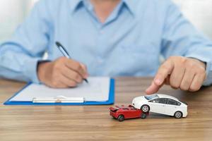 Car insurance concept , A man use a pen write insurance document on table and accident toy car model concept on wood table photo