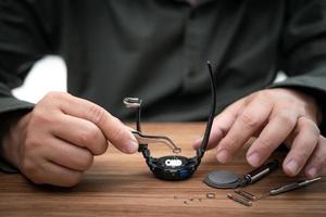 A man use pliers to clamp the digital watch battery remove and change in repairing broken wristwatches and tool on wood table photo