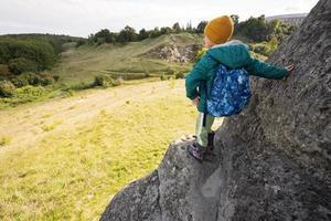 Boy with backpack climbing big stone in hill. Pidkamin, Ukraine. photo