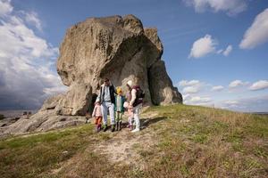 Family exploring nature. Children with parents wear backpack hiking against big stone in hill. Pidkamin, Ukraine. photo