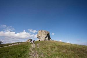 Kids exploring nature. Children wear backpack hiking with mother near big stone in hill. Pidkamin, Ukraine. photo