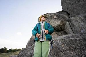 Boy with backpack climbing big stone in hill. Pidkamin, Ukraine. photo