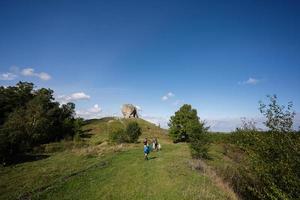 Kids exploring nature. Children wear backpack hiking with mother near big stone in hill. Pidkamin, Ukraine. photo