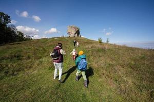 niños explorando la naturaleza. los niños usan mochilas de senderismo con la madre cerca de una gran piedra en la colina. pidkamin, ucrania. foto