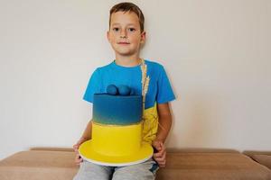 niño ucraniano celebrando cumpleaños sosteniendo un gran pastel con bandera de ucrania. foto