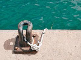 Rusty mooring bollard with a rope on a concrete pier photo