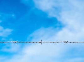 One strand of a barbed wire with blue sky and clouds in the background. photo