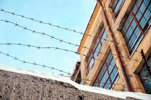 Barbed wire on a fence in snow with an old factory and blue sky on a background photo