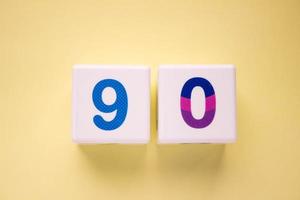 Close-up photo of a white plastic cubes with a colorful number 90 on a yellow background. Object in the center of the photo