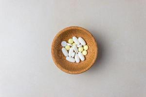 A handful of pills in a wooden plate. The concept of medcine, treatment. Top view photo