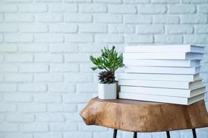 pila de libros blancos en blanco para maquetas y macetas suculentas blancas sobre una mesa moderna de madera foto