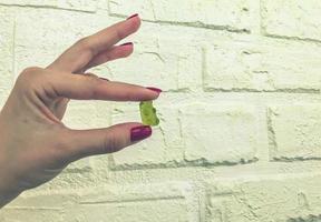 a gummy yellow bear in the hands of a girl with a red manicure. bear are kept on a white brick background. high-calorie homemade dessert made from fruit juices and nectars, a natural product photo