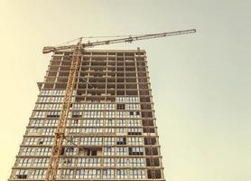 a tall glass house, partly without windows and doors. the house is being built with a construction crane. urban landscape. erection of walls and floors in a high-rise photo