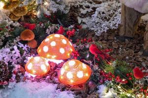 Christmas decor for a shopping center. cute amanita mushrooms with lights inside. next to them are red birds made of artificial materials. cute spruce branches in the center photo