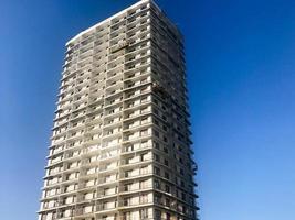 Large high reinforced concrete, panel, monolithic frame, frame-block house, building, skyscraper, new building with a glare of the sun in the windows against the blue sky photo