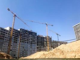 Building with the help of construction cranes of high reinforced concrete, panel, cast-frame, frame-block houses, buildings, skyscrapers, new buildings on the background of sandy land photo