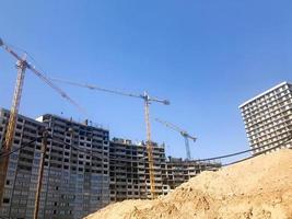 Building with the help of construction cranes of high reinforced concrete, panel, cast-frame, frame-block houses, buildings, skyscrapers, new buildings on the background of sandy land photo