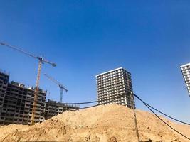 Building with the help of construction cranes of high reinforced concrete, panel, cast-frame, frame-block houses, buildings, skyscrapers, new buildings on the background of sandy land photo