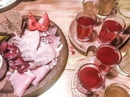 Meat snack with alcohol made from meat, ham, basturma with sauce and many glasses, shots with strong alcohol, vodka, filling on wooden stands on a table in a cafe, bar, restaurant photo