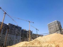 Building with the help of construction cranes of high reinforced concrete, panel, cast-frame, frame-block houses, buildings, skyscrapers, new buildings on the background of sandy land photo