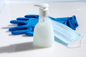 Blue rubber gloves, medical face mask and soap bottle on a light background. photo