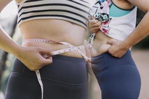 hermosa mujer gorda con cinta métrica usa su mano para exprimir el exceso de grasa que está aislado en un fondo blanco. ella quiere perder peso, el concepto de cirugía y descomponer grasa bajo el foto