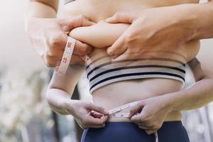 hermosa mujer gorda con cinta métrica usa su mano para exprimir el exceso de grasa que está aislado en un fondo blanco. ella quiere perder peso, el concepto de cirugía y descomponer grasa bajo el foto