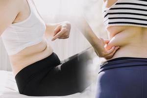 hermosa mujer gorda con cinta métrica usa su mano para exprimir el exceso de grasa que está aislado en un fondo blanco. ella quiere perder peso, el concepto de cirugía y descomponer grasa bajo el foto