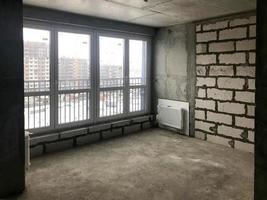 The apartment in the new building with a free layout without repair and decoration with bare walls and a large panoramic French window on the whole wall. Concept repair, housewarming, building photo