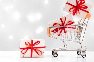 Holiday shopping. Mini cart with gifts on white background with lights. photo