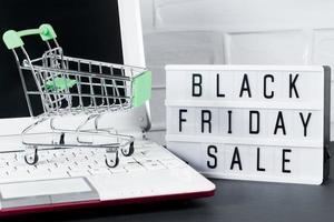 Black Friday concept. Mini shopping cart and laptop. Online sale and discount. photo