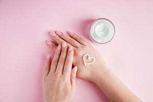 A young woman is applying cream to her hands. Spa and body care concept on a pink background. Image for advertising. photo