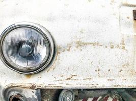 An old retro vintage hipster rusty oxidized chrome-plated metallic silver radiator grille and a round glass retro spotlight of an antiquan white white American car from the 60s, 70s, 80s, 90s, 2000s photo