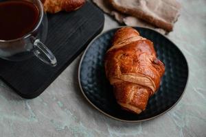 Delicious crispy croissant with chocolate with a cup of invigorating coffee on a light concrete background photo